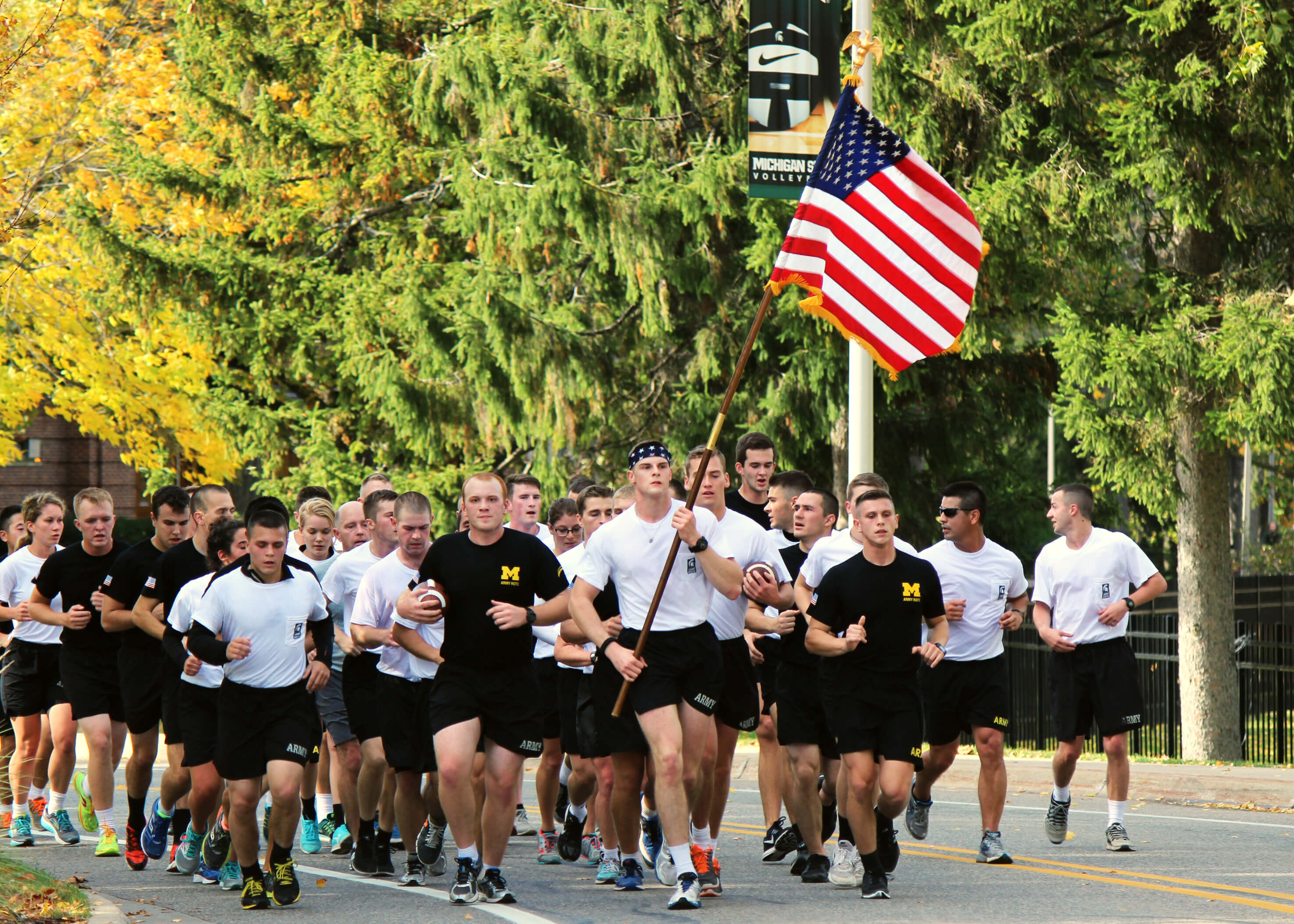 A team of football players running together carrying an American flag