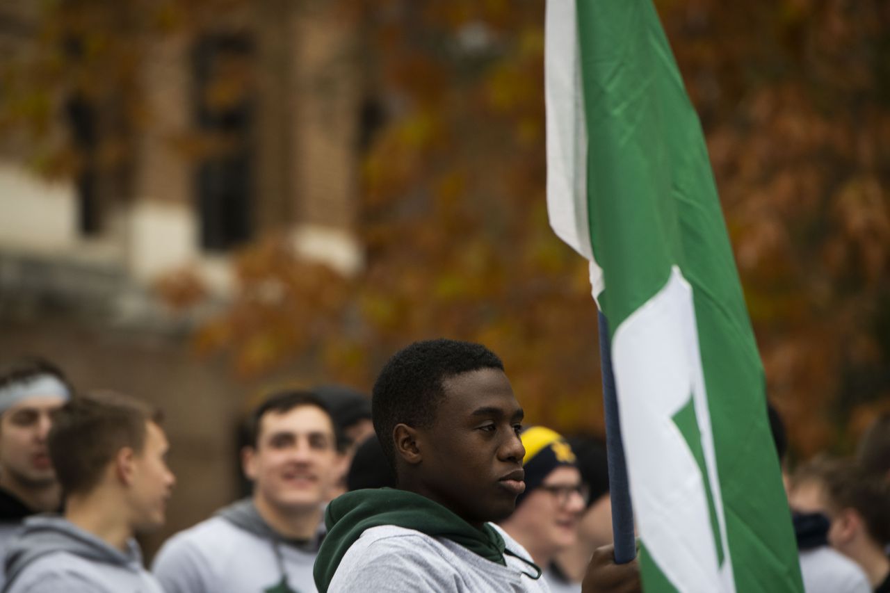 Alassane Gueye holds a Michigan State flag while waiting to run the final mile with other members of the University of Michigan and Michigan State ROTC programs during the annual Alex's Great State Race on Friday Nov. 15, 2019. Cadets carried the game ball for 64 miles in honor of Alex Powell, an MSU student that passed away in 2011. Nicole Hester/Mlive.com