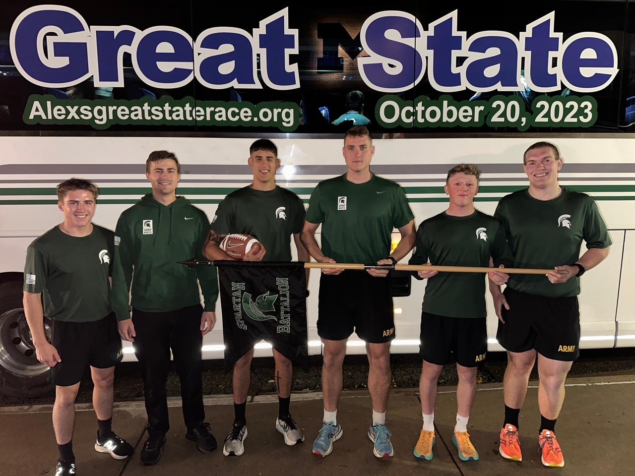 A group of MSU cadets standing in front of AGSR bus holding game ball before the start of the race