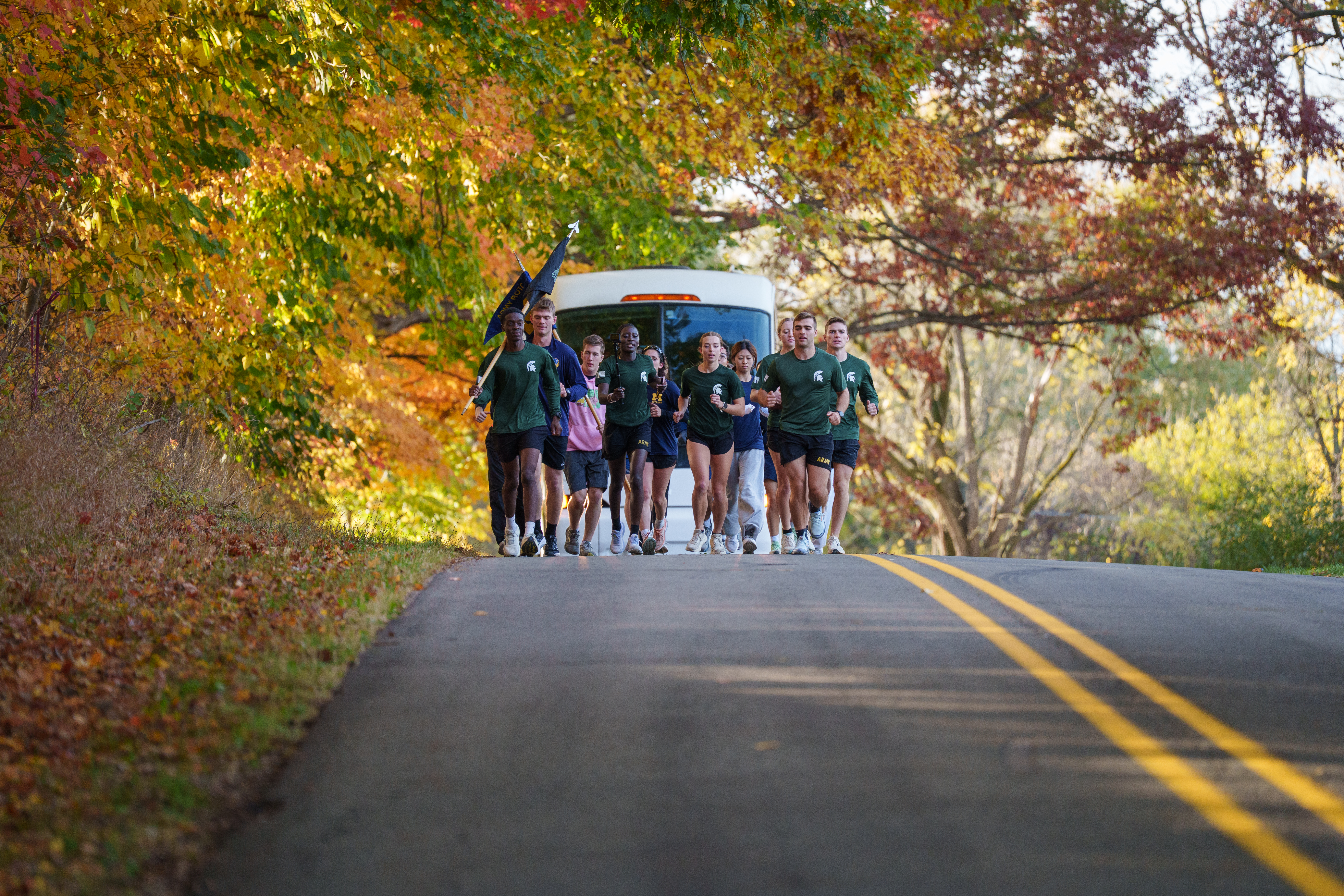 ROTC Cadets from MSU and UM running along the road with a Dean Trailways bus behind them
