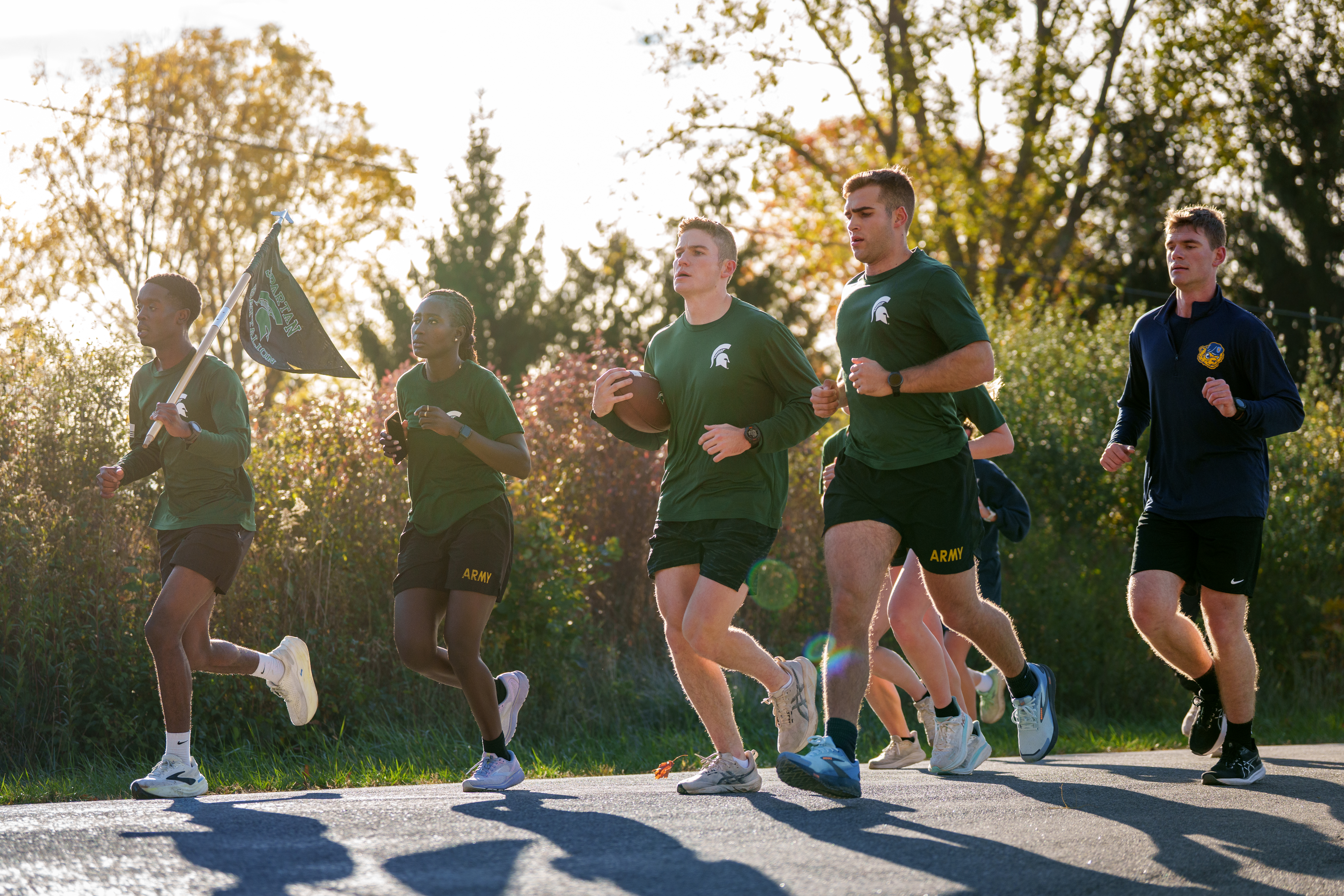 UM and MSU runners carrying flags and game ball on backroad