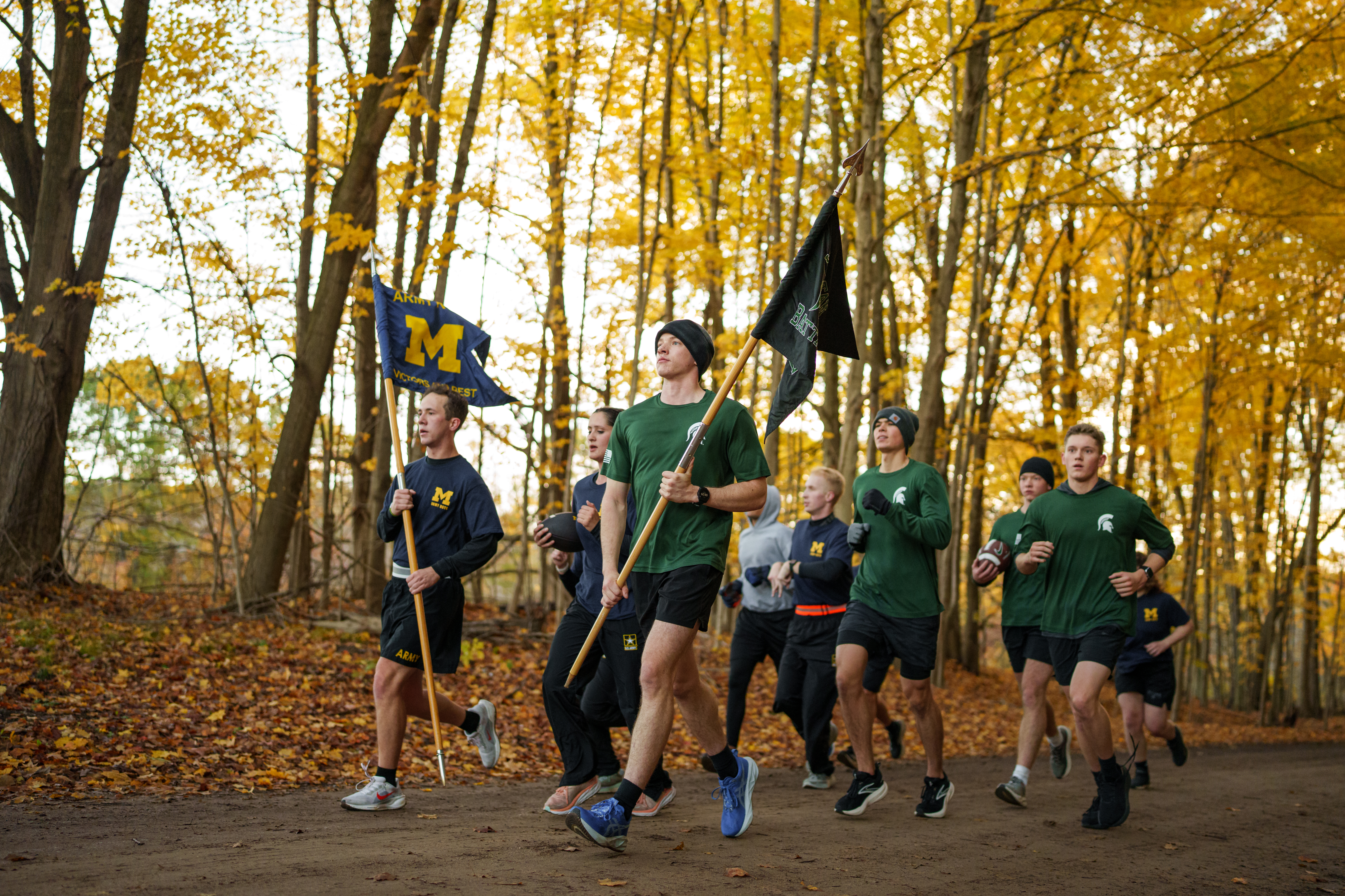 ROTC Cadets from MSU and UM carrying flags and running on a brisk fall day.