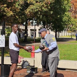 ROTC cadet presenting official game ball to Martino Harmon, VP of Student Affairs at UM