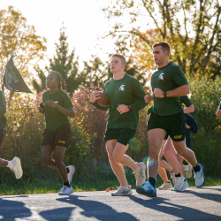 UM and MSU runners carrying flags and game ball on backroad