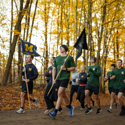 ROTC Cadets from MSU and UM carrying flags and running on a brisk fall day.