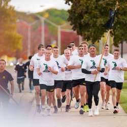 One MSU cadet holding flags and game ball running toward finish line